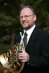Gordon James, a whote man with glasses and a beard holding his instrument and wearing a suit