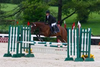 Angela DeBoer, wearing a horse riding uniform and riding a brown horse mid jump over a hurdle