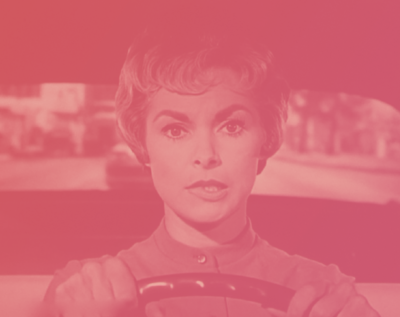 Red tinted image of actress Janet Leigh driving a car biting her lip