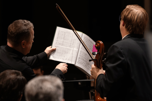 The conductor using his baton to point at the musi csheet while a violinist looks