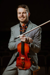Josh Holritz, a white man with short brown hair and a beard wearing a grey suit and holding his instrument