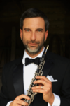 Carey Shinbaum, a white man with short dark hair and a beard, posing with his instrument and wearing a suit